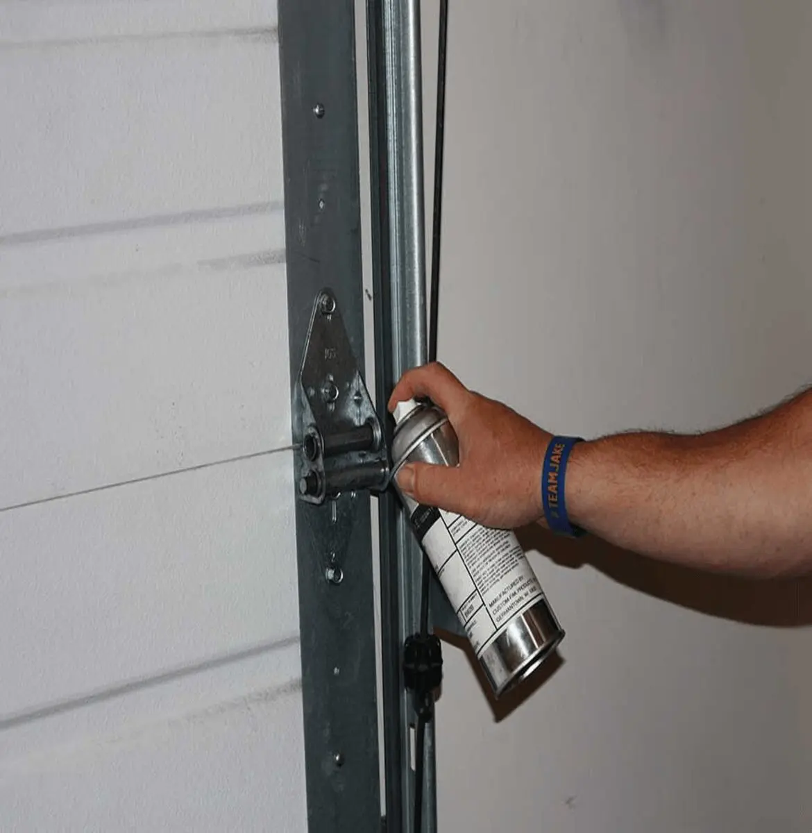 Hand spraying lubricant on a door hinge.